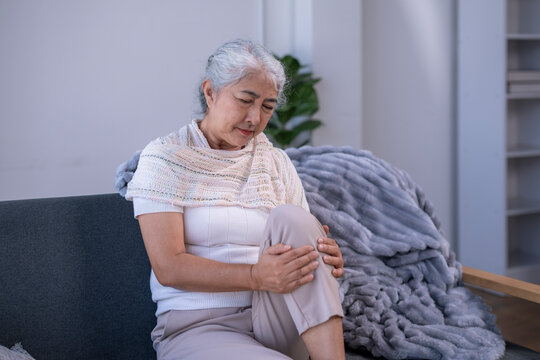 Senior woman feeling knee pain on couch