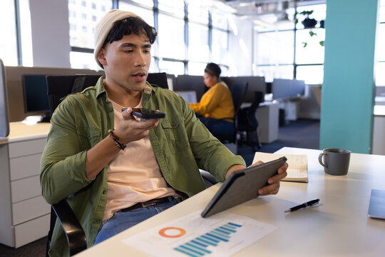 Diverse coworkers collaborating at open plan office desk, using tablet and smartphone, copy space