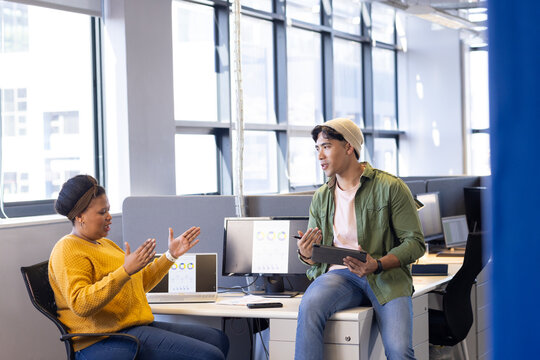 Diverse coworkers in business casual discussing data charts on monitors and tablet at modern office