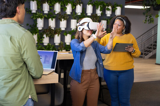 Diverse coworkers collaborating on virtual reality headset demo in office with laptop and tablet