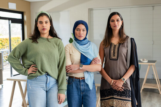 Diverse female coworkers standing wearing blue hijab with wooden tables in modern meeting room