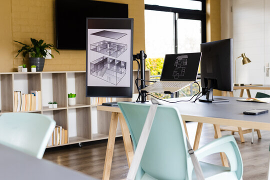Workstation featuring dual monitors and laptop displaying plans on desk with mint-green chairs