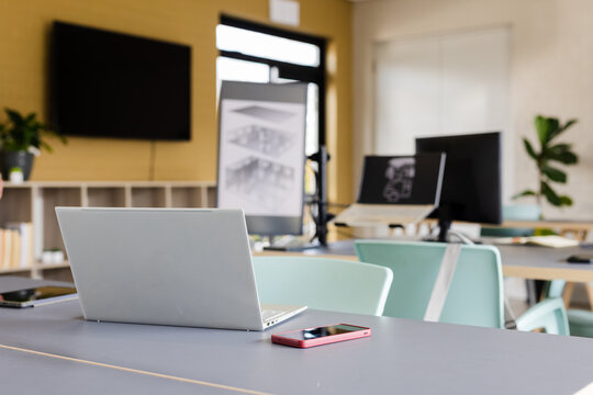 Open silver laptop resting on meeting table with red smartphone and whiteboard sketches behind