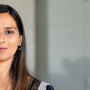 Indian woman posing before light-gray wall, displaying bindi and gold hoop earring, copy space
