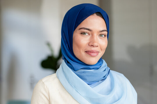 Indian female standing in living area wearing gradient blue hijab, cream sweater showing nose stud