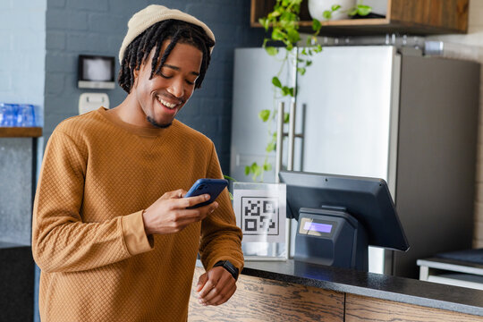 African American man scanning acrylic QR code using smartphone at cafe counter with POS screen