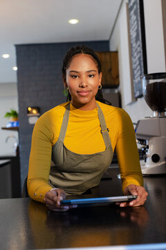 African American woman barista holding tablet at coffee bar beside espresso grinder chalkboard menu