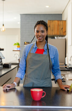 African American woman barista in apron placing latte foam in red mug on counter in cafe