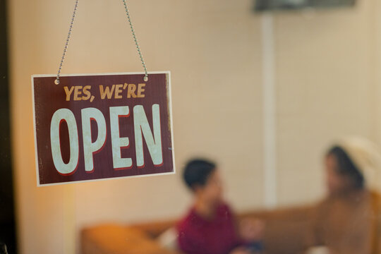 Diverse friends sitting on sofa in cafe behind storefront window chatting near open sign and chain