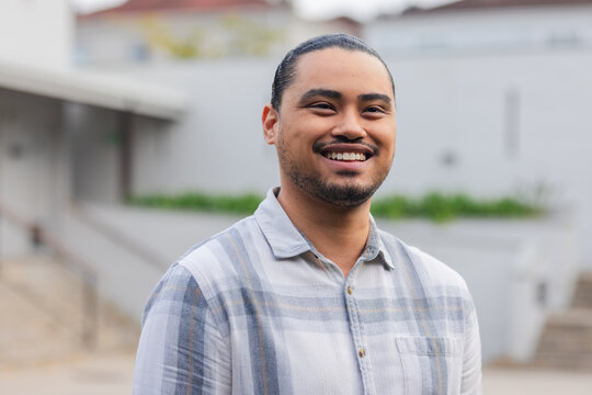 Asian man standing in courtyard wearing plaid shirt holding railing near planters and stone steps