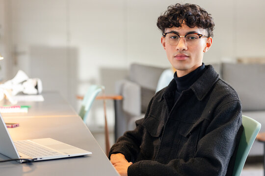 Asian man typing on silver laptop at lounge study area with smartphone and notebooks, copy space