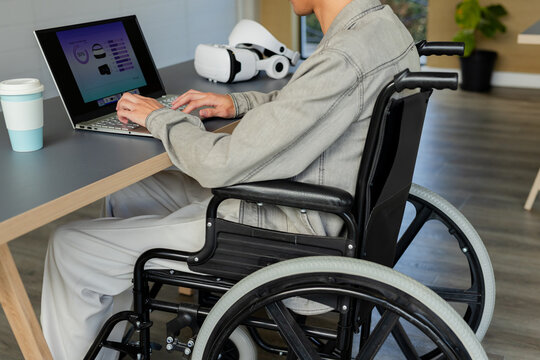 Laptop displaying data charts and VR headset sitting on wood office desk near manual wheelchair