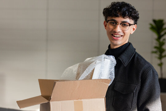 Man wearing jacket unpacking box with bubble wrap at office with potted plant, copy space