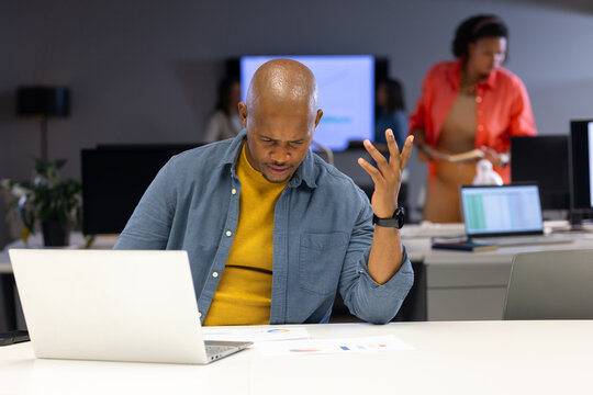 African American coworkers at desk, man making frustrated gesture while colleague holding paperwork