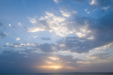 Obraz premium Gentle sun setting beneath scattered clouds casts pastel hues across the calm Mediterranean waters near Oristano, Sardinia. The peaceful sky and subtle light create an airy, serene atmosphere.