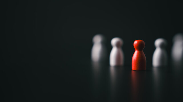 Red wooden pawn standing out from blurred white figures in dark background symbolizing leadership bold decision making individuality and strategic vision