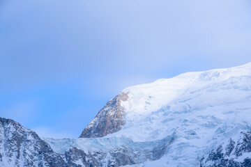 Obraz premium Soft morning light illuminates the icy slopes and rugged rock of Mont Blanc du Tacul, with crisp snow and a serene blue sky creating a peaceful alpine atmosphere.