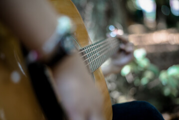 Person playing acoustic guitar outdoors among blurred green foliage and warm sunlight