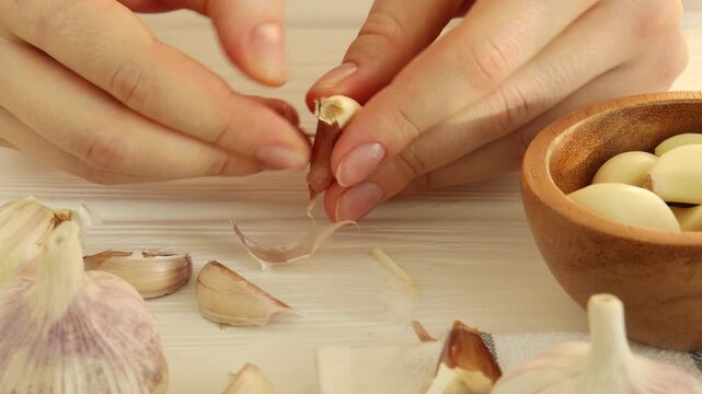Woman peeling fresh garlic at white wooden table, closeup