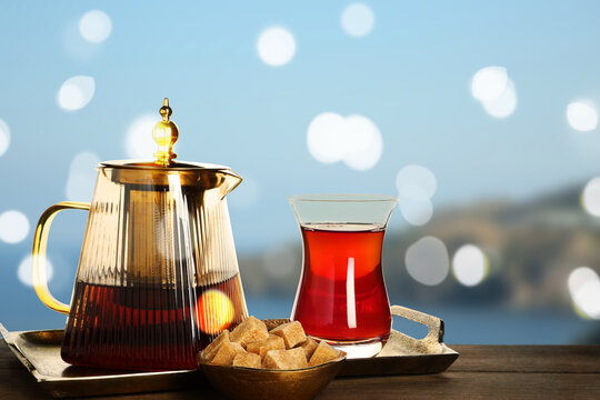Traditional Turkish tea and sugar on wooden table against blurred seascape