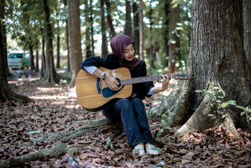 Woman in hijab playing acoustic guitar in forest