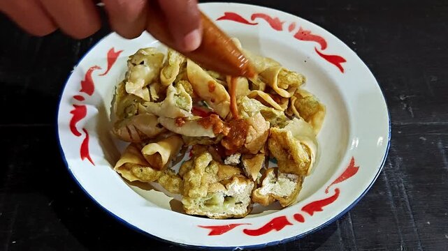 Pouring Savory Peanut Sauce Over Crispy Batagor Indonesian Fried Fish Dumplings and Tofu