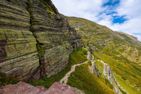 A dramatic cliffside section of the Highline Trail in Glacier National Park, featuring rugged rock formations and hikers along a narrow path.