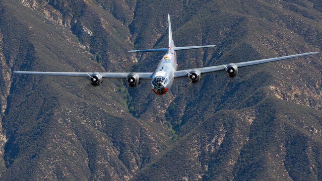 Front view of a rare WWII bomber (B-29 Superfortress) flying over hills