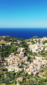 Aerial view of Corbara village with traditional Mediterranean houses and the deep blue sea in Corsica, France. Bright sunny day highlights the coastal landscape and charming architecture.