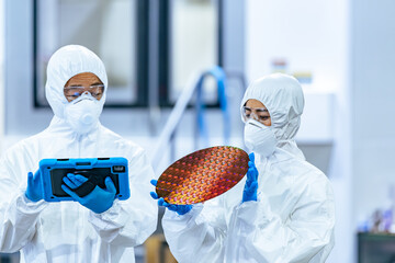 半導体工場でタブレットを持ってシリコンウエハーを検査する防護服を着た男女作業員