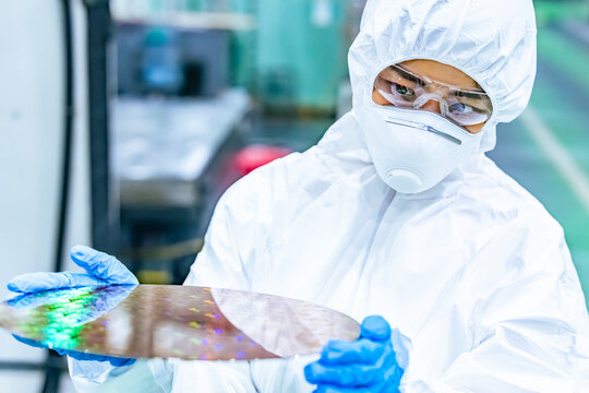 半導体工場でシリコンウエハーを検査する防護服を着た女性作業員