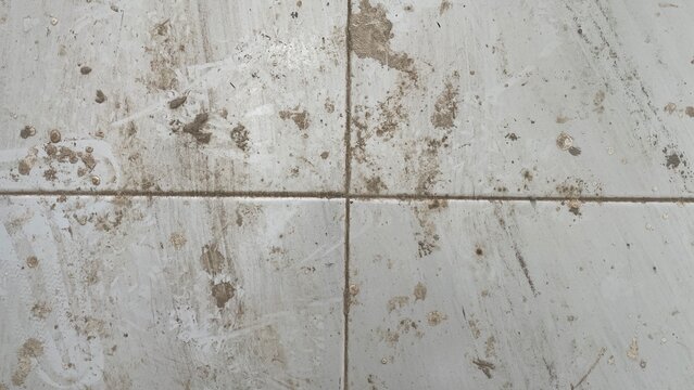 Dirty white floor tiles covered in muddy stains and grime, showcasing a messy and unhygienic surface in need of cleaning.