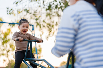 Obraz premium cheerful child girl and mother playing seesaw in playground