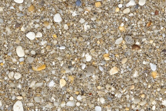 Close-up view of varied pebbles and sand on a beach. Seamless pattern.