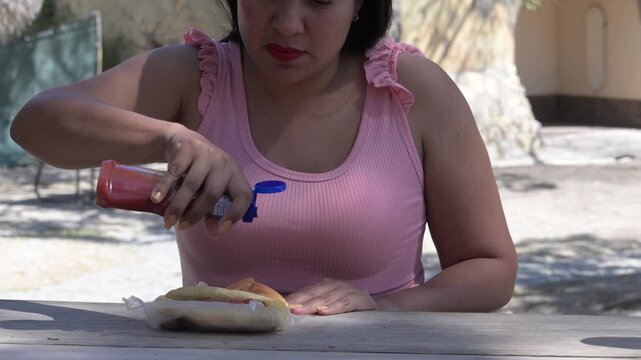Latina woman putting ketchup on her hot dog.