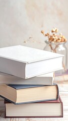 Stack of books sits on wooden table with dried flowers against a textured wall