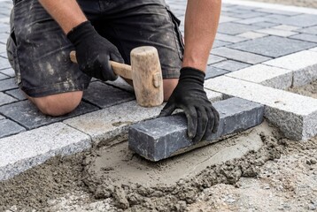 Construction worker placing a stone paver with a hammer