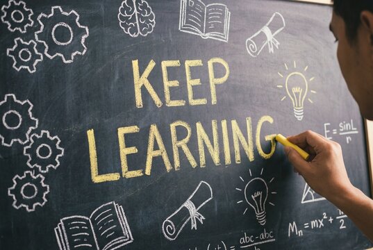 Hand writing KEEP LEARNING in yellow chalk on a chalkboard