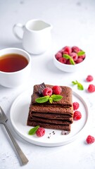 Stacked chocolate crepes adorned with raspberries & mint, tea and cream on white
