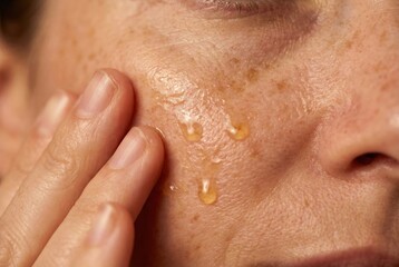Fototapeta premium Woman massaging golden Vitamin C serum into sun-damaged skin