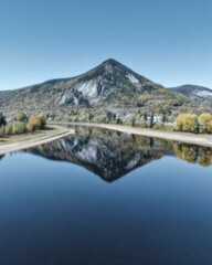 Majestic mountain peaked summit reflecting in calm river water with autumn foliage during fall season in a scenic valley landscape with blue sky and copy space