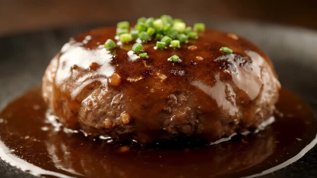 Juicy Hamburg Steak (Hambagu) close-up view, generously coated with rich demi-glace sauce and garnished with chives, served on a gourmet black dish.
