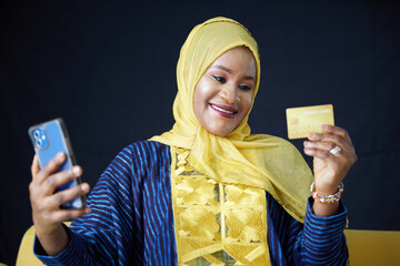 Muslim woman using a smartphone and holding a credit card on black background