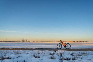 mountain bike at winter sunset on a biking trail with field covered by snow and industrial area in background