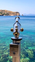 Seaside coin operated telescope stands over turquoise water with rocky headland view