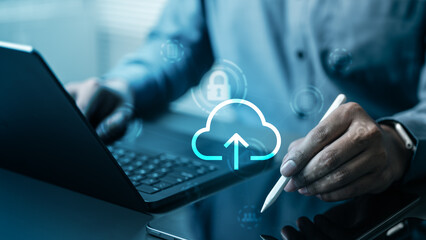 Business professional using laptop and tablet with cloud upload icon, representing secure cloud...