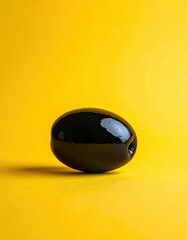 Single Glossy Black Olive With Water Droplets Rests On A Vibrant Yellow Background With Subtle Shadows And Highlights