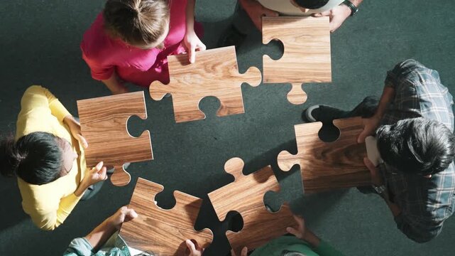 Top down view of business people gathering jigsaw together at meeting. Aerial view of diverse team collect or put piece of jigsaw puzzle together and standing while wearing casual cloth. Symposium.