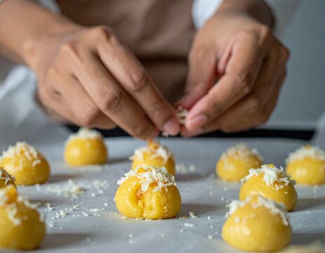 Close up of baker hands decorating raw nastar dough with shredded cheese topping on a baking tray