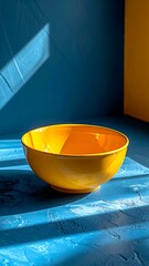 Bright yellow bowl on blue surface, sunlit with shadows. Strong contrast and geometric backdrop